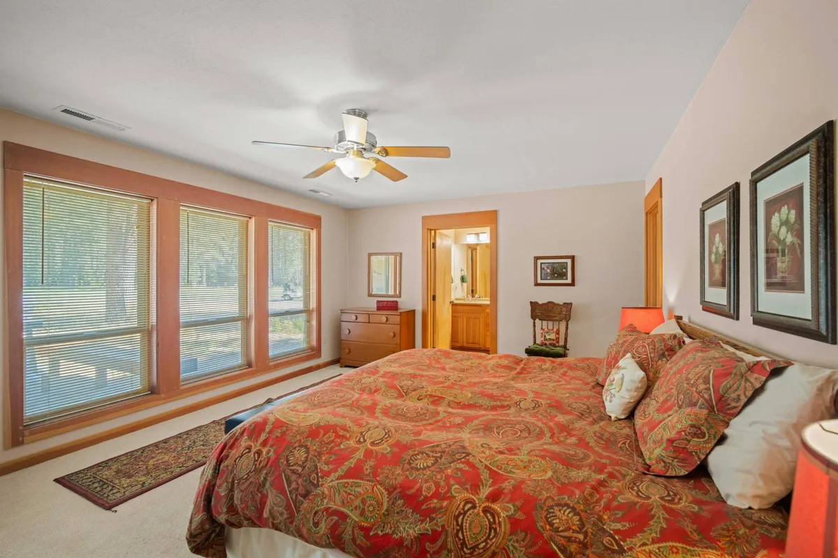 A cozy bedroom with a bed adorned with patterned bedding, large windows that let in abundant natural light, wooden furniture, and decorative artwork. The space feels warm, peaceful, and perfectly suited for unwinding.