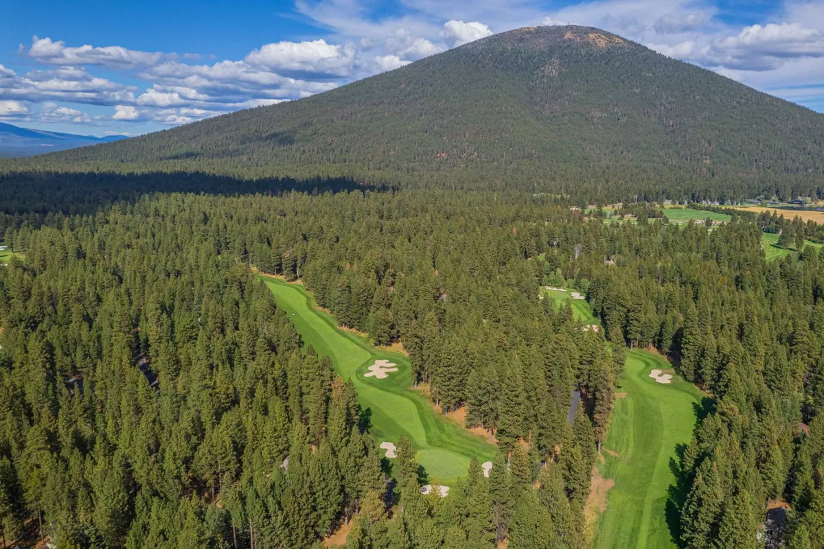 This exterior image presents a sweeping view of a lush golf course set against a dramatic mountain backdrop, bordered by dense forest. Golfers can be seen enjoying a relaxed day on the green, while the serene environment invites leisurely walks and nature exploration.