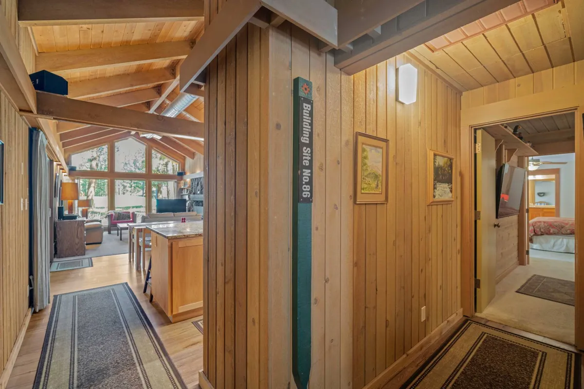 A cozy seating area framed by exposed wooden beams and expansive windows. Art on the walls and plush furnishings create a welcoming vibe, while the windows offer scenic views, likely over the golf course.