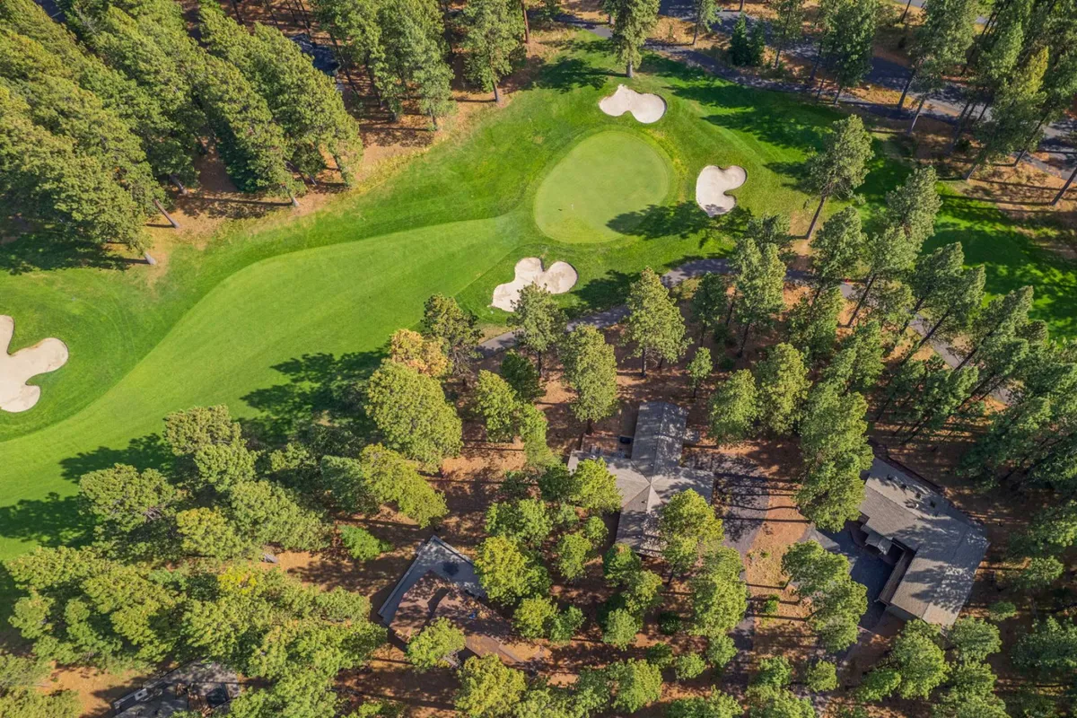 This image provides a sweeping view from the residential property across the third green of the Big Meadow Golf Course, framed by sand traps, manicured fairways, and stately pine trees. The peaceful setting is ideal for enjoying nature and the serene golf course views from the deck or patio.