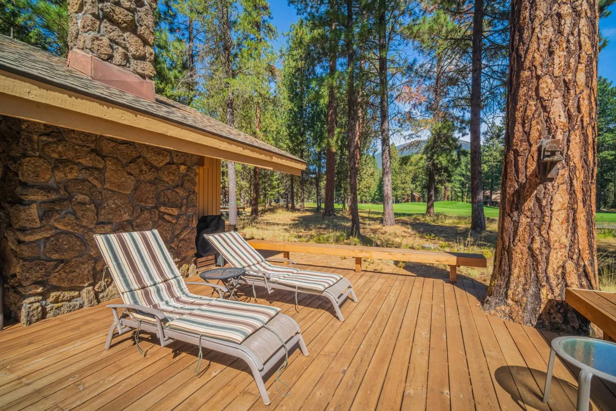 A serene deck area outfitted with lounge chairs, a stone wall, and surrounded by tall trees. The scene is tranquil and inviting, ideal for relaxing after a day of exploring the outdoors with your pet.