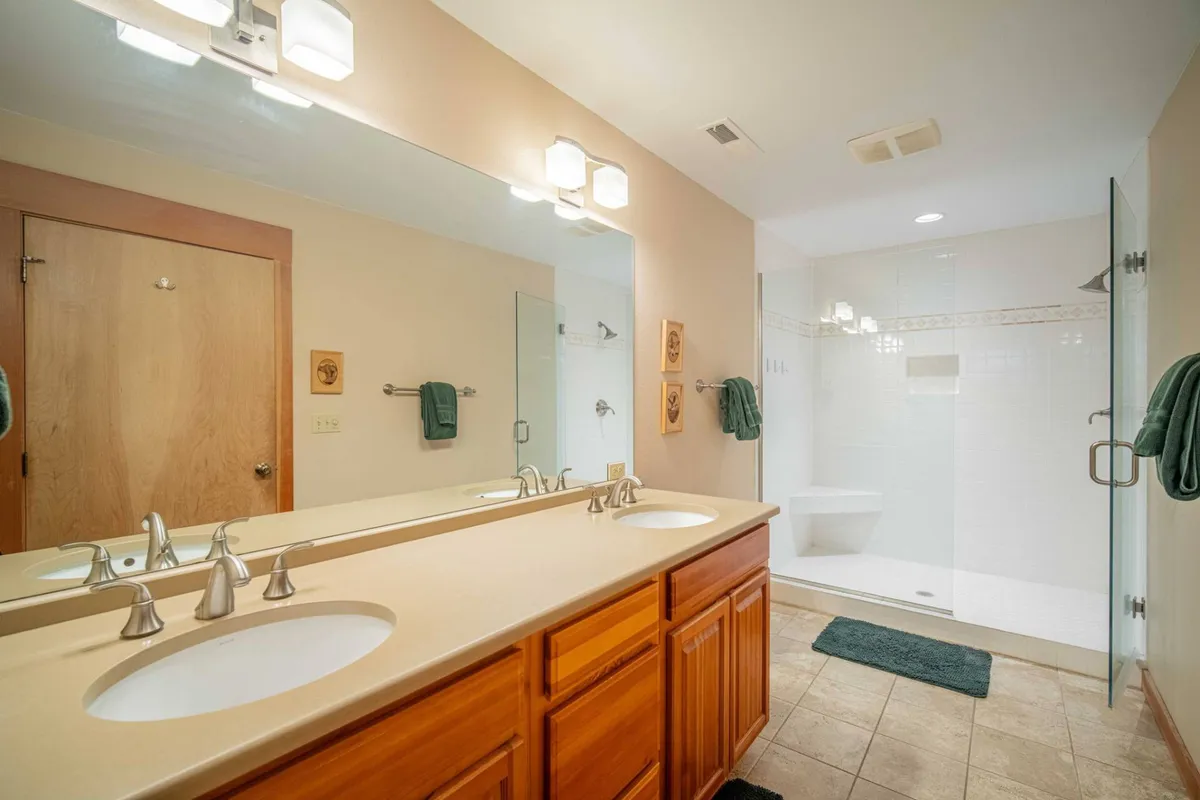 A modern en-suite bathroom boasting double vanity sinks, a glass shower enclosure, and elegant wooden cabinetry. The zen-like ambiance creates an inviting space for both morning routines and evening relaxation.