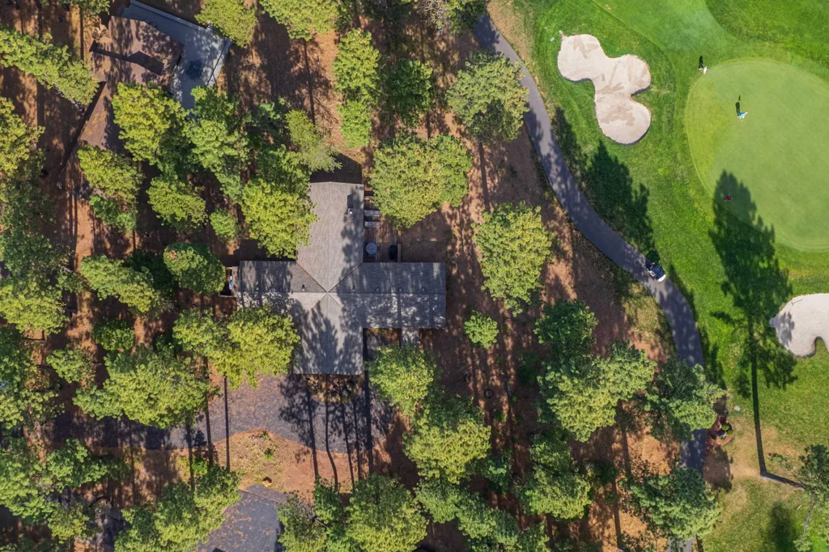 This image captures a home directly facing a lush golf course, surrounded by tall trees, with the green stretching invitingly into the distance. The house and patio are clearly visible, offering a tangible connection between the private residence and the golf course beyond.